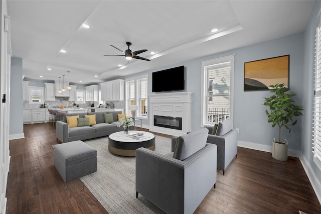 living room featuring dark wood-type flooring, a glass covered fireplace, baseboards, and recessed lighting