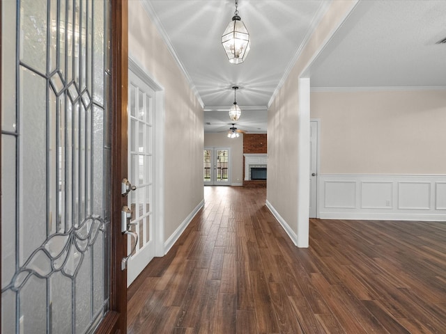 foyer with a decorative wall, a wainscoted wall, dark wood-style flooring, a brick fireplace, and crown molding