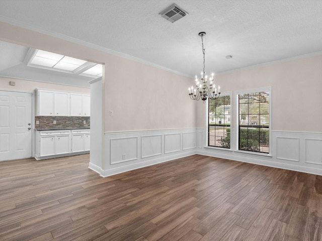 unfurnished dining area featuring a textured ceiling, a notable chandelier, wood finished floors, visible vents, and crown molding