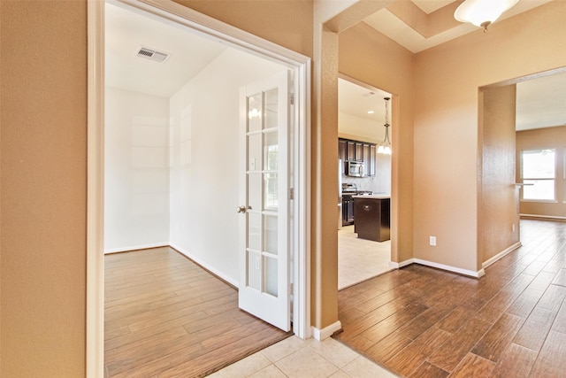 hallway featuring light wood-type flooring, baseboards, and visible vents