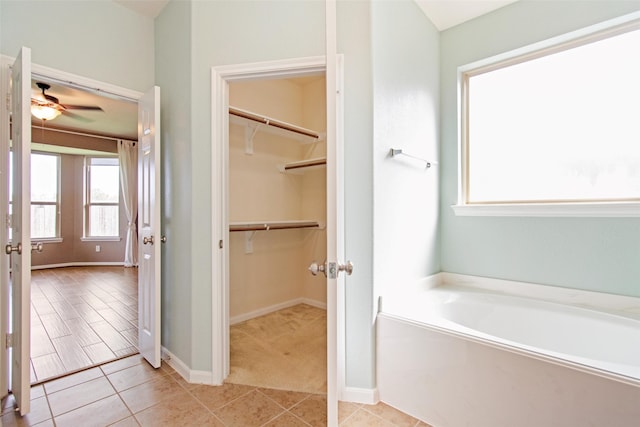 full bath featuring ceiling fan, tile patterned flooring, baseboards, a bath, and a walk in closet