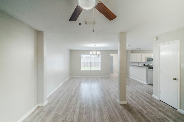 unfurnished living room with ceiling fan with notable chandelier, light wood-type flooring, visible vents, and baseboards