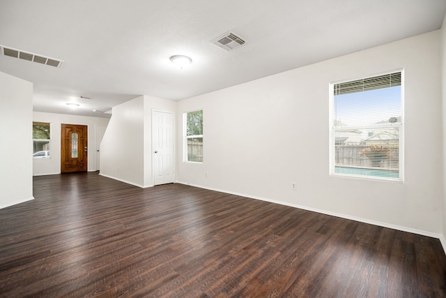 empty room with dark wood-type flooring, visible vents, and baseboards