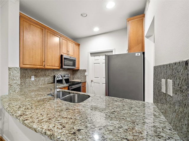 kitchen featuring stainless steel appliances, recessed lighting, a sink, light stone countertops, and a peninsula