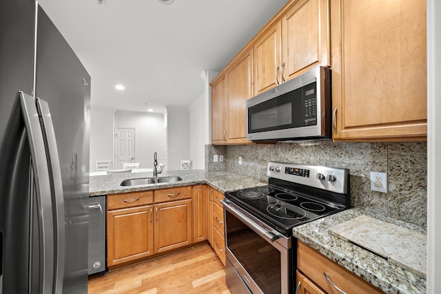 kitchen with light wood-style floors, appliances with stainless steel finishes, light stone counters, and a sink