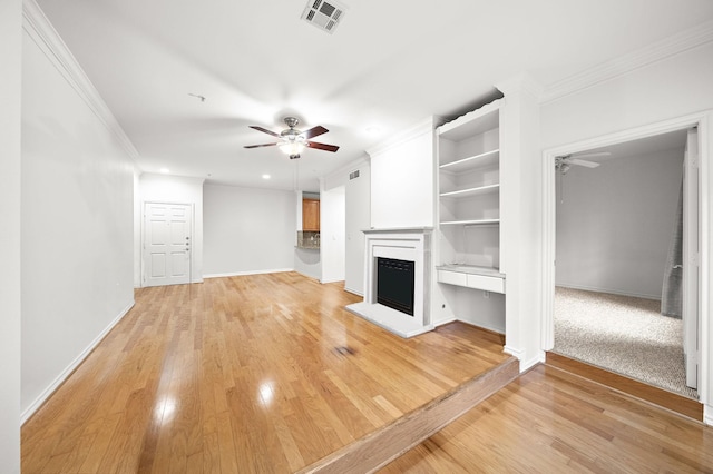 unfurnished living room with a fireplace with raised hearth, ceiling fan, ornamental molding, and visible vents