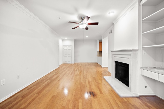 unfurnished living room with light wood-type flooring, a ceiling fan, crown molding, and a glass covered fireplace