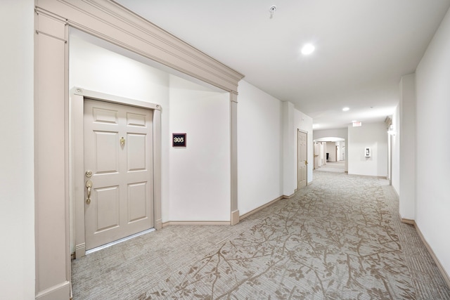 corridor featuring arched walkways, recessed lighting, baseboards, and light colored carpet