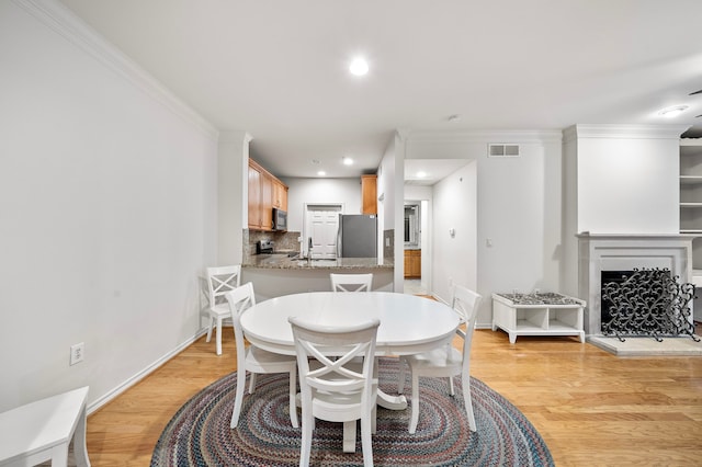 dining space featuring a fireplace with raised hearth, light wood finished floors, visible vents, and crown molding