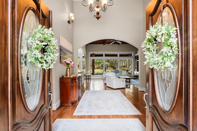 entryway with light wood-style floors, arched walkways, a chandelier, and baseboards