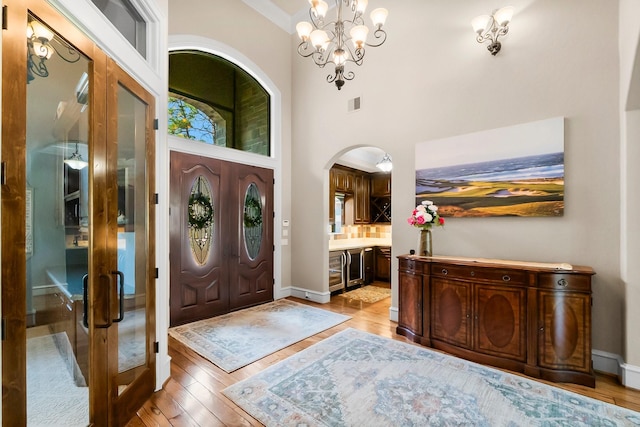 foyer with arched walkways, a towering ceiling, light wood-style flooring, and baseboards