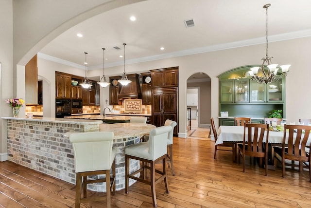 kitchen with visible vents, arched walkways, light wood-style flooring, and pendant lighting