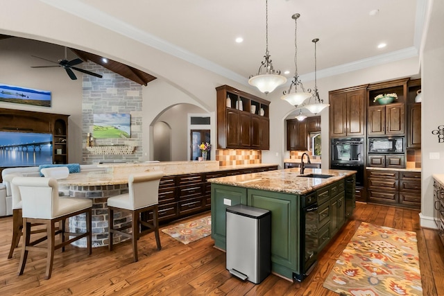 kitchen featuring arched walkways, an island with sink, hanging light fixtures, dark brown cabinets, and black appliances