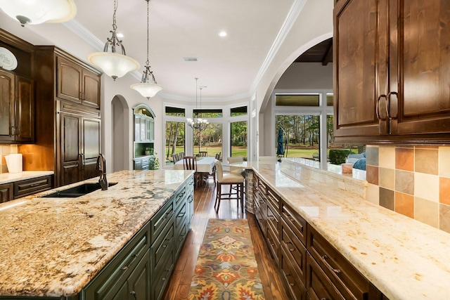 kitchen with light stone counters, dark wood finished floors, crown molding, a center island with sink, and a sink