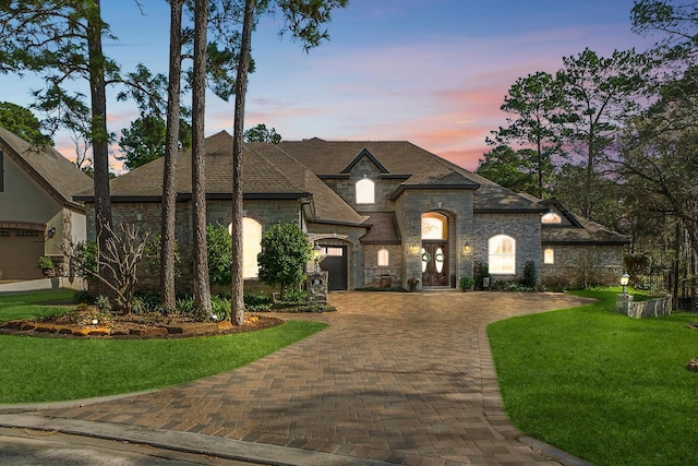 french country home with a yard, decorative driveway, and stone siding