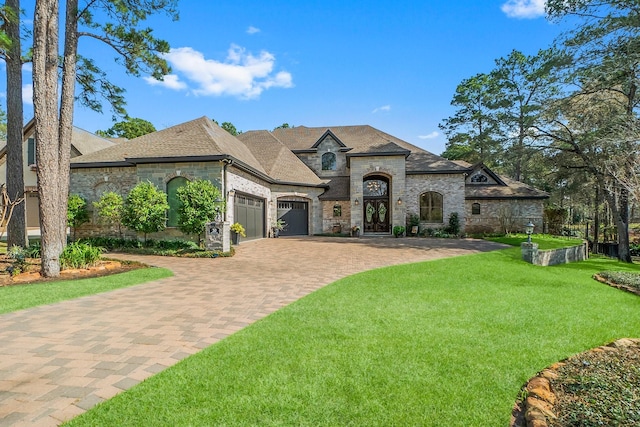 french country inspired facade featuring a garage, a shingled roof, stone siding, decorative driveway, and a front lawn