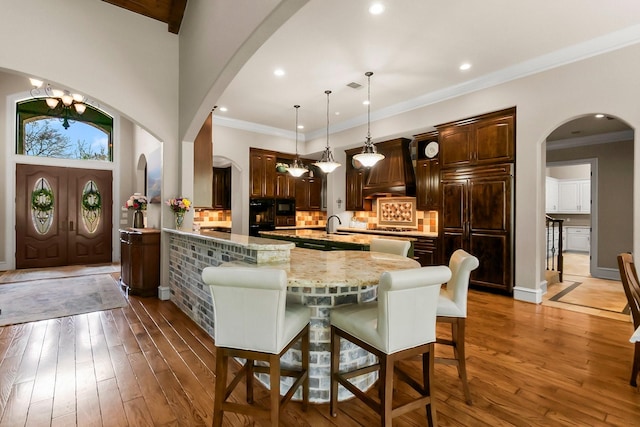 kitchen with dark wood-style floors, a large island, custom range hood, paneled built in refrigerator, and crown molding