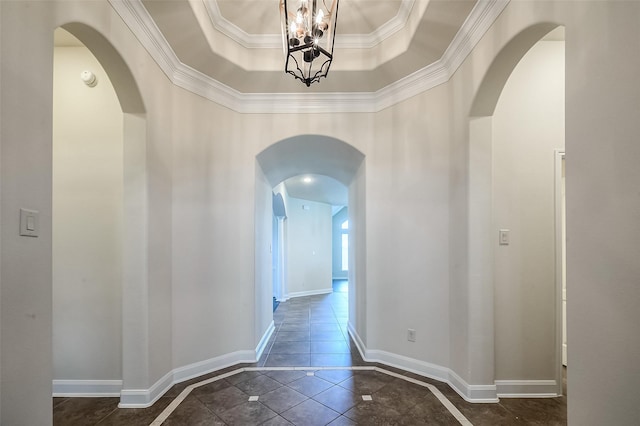 hallway featuring baseboards, a raised ceiling, and arched walkways