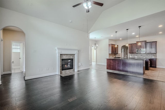 kitchen featuring arched walkways, pendant lighting, stainless steel microwave, open floor plan, and a kitchen island with sink