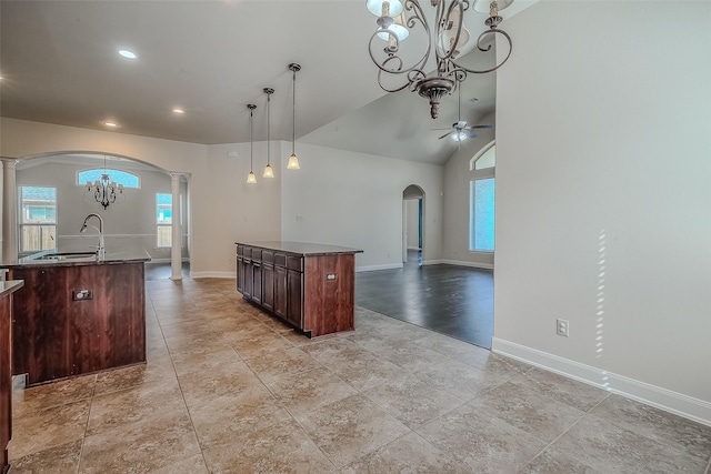 kitchen featuring arched walkways, ceiling fan with notable chandelier, open floor plan, dark countertops, and a center island with sink