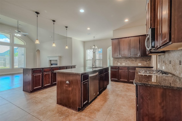 kitchen with a kitchen island with sink, ceiling fan with notable chandelier, appliances with stainless steel finishes, tasteful backsplash, and decorative light fixtures