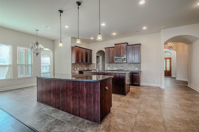 kitchen with arched walkways, a notable chandelier, a sink, stainless steel microwave, and decorative light fixtures