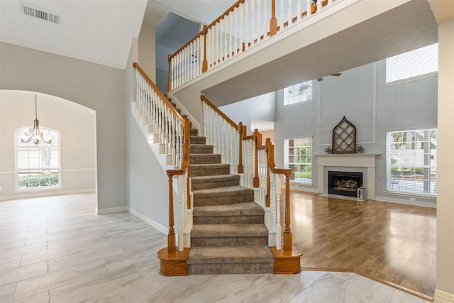 staircase featuring visible vents, a high ceiling, a fireplace with flush hearth, wood finished floors, and baseboards