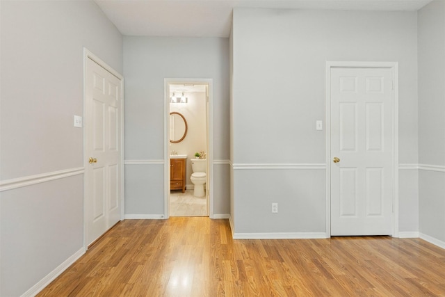 unfurnished bedroom with connected bathroom, light wood-style flooring, and baseboards