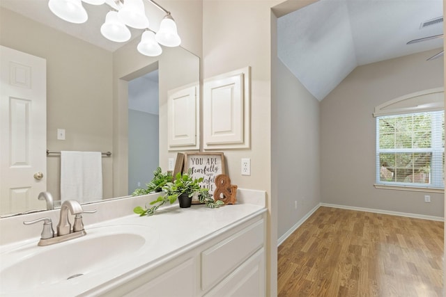 bathroom with wood finished floors, vanity, visible vents, vaulted ceiling, and baseboards