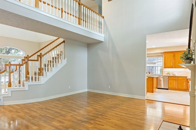 unfurnished living room featuring recessed lighting, a high ceiling, baseboards, stairway, and light wood finished floors