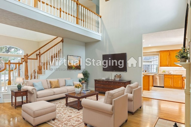 living room featuring stairs, a high ceiling, light wood-type flooring, and baseboards