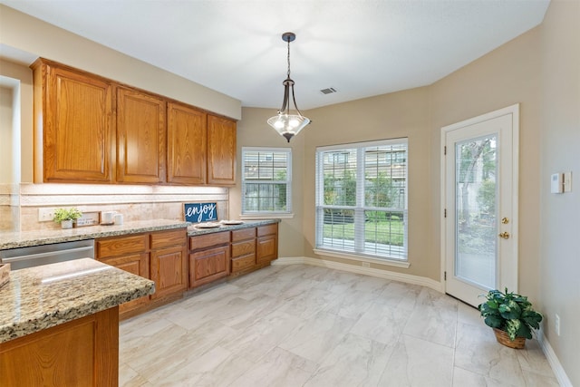 kitchen featuring hanging light fixtures, stainless steel dishwasher, brown cabinets, light stone countertops, and tasteful backsplash