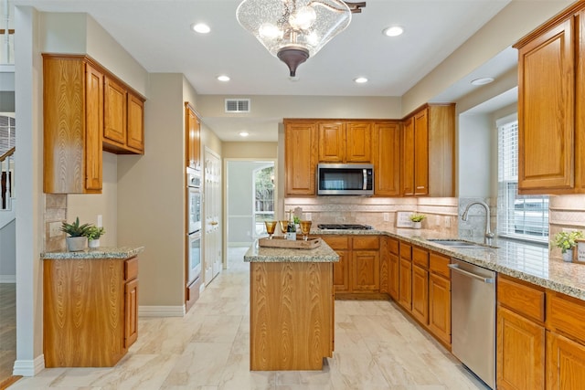 kitchen featuring brown cabinets, visible vents, appliances with stainless steel finishes, a kitchen island, and light stone countertops