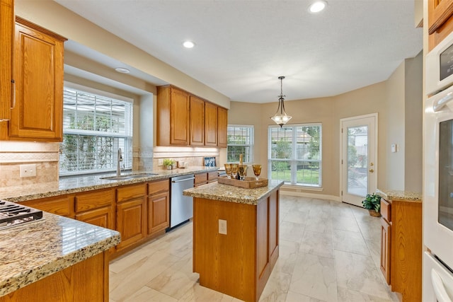 kitchen featuring hanging light fixtures, appliances with stainless steel finishes, brown cabinetry, a sink, and a kitchen island