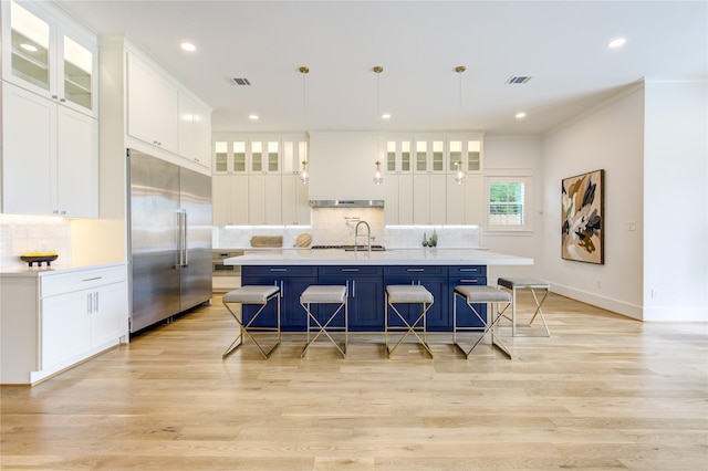 kitchen with a breakfast bar, pendant lighting, light countertops, an island with sink, and stainless steel built in refrigerator