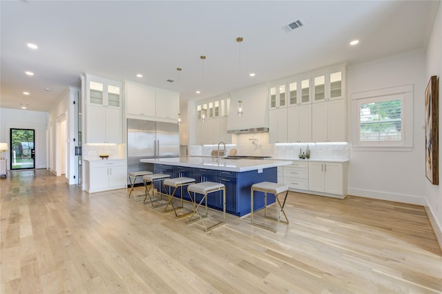 kitchen with visible vents, a breakfast bar area, a kitchen island with sink, light countertops, and built in fridge