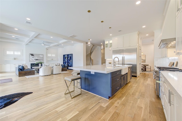 kitchen featuring pendant lighting, a center island with sink, light countertops, open floor plan, and white cabinetry