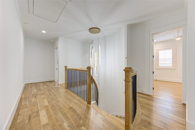 hall featuring an upstairs landing, baseboards, light wood-style floors, attic access, and crown molding