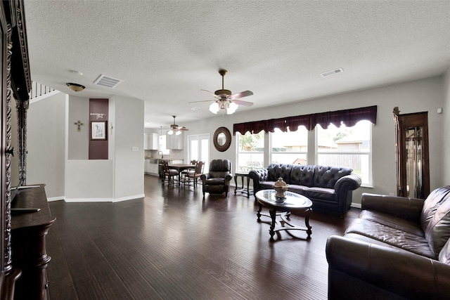 living room with dark wood-style floors, a textured ceiling, visible vents, and baseboards