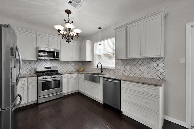 kitchen featuring a sink, visible vents, hanging light fixtures, appliances with stainless steel finishes, and dark wood-style floors