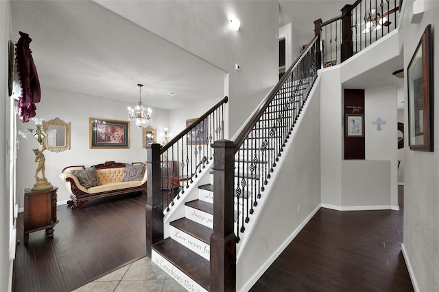 staircase featuring a notable chandelier, a towering ceiling, baseboards, and wood finished floors