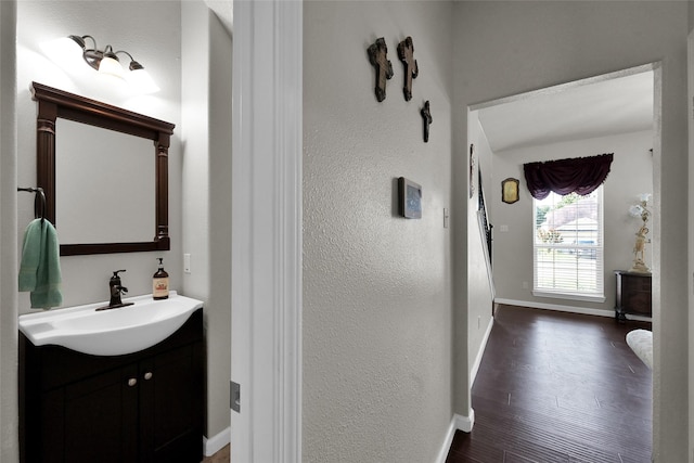 half bath featuring vanity, baseboards, and wood finished floors