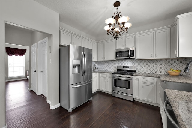 kitchen featuring pendant lighting, dark wood-style flooring, appliances with stainless steel finishes, white cabinets, and light stone countertops