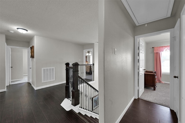 hallway with a textured ceiling, dark wood-style flooring, visible vents, an upstairs landing, and attic access