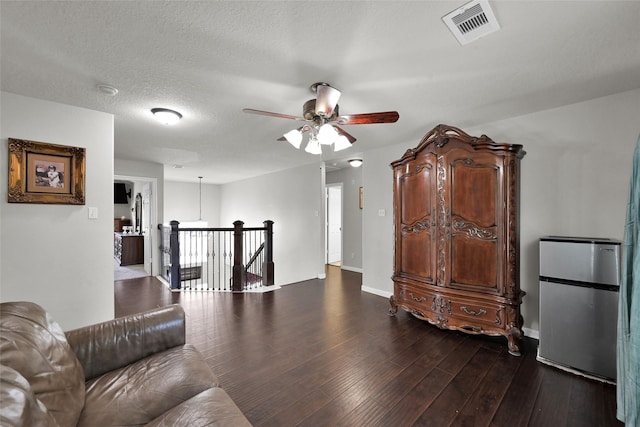 living room featuring baseboards, visible vents, a ceiling fan, dark wood finished floors, and a textured ceiling