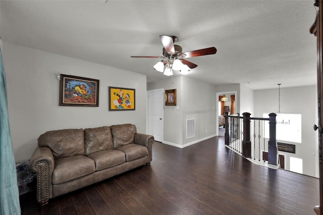 living room with baseboards, visible vents, dark wood-type flooring, a textured ceiling, and ceiling fan with notable chandelier