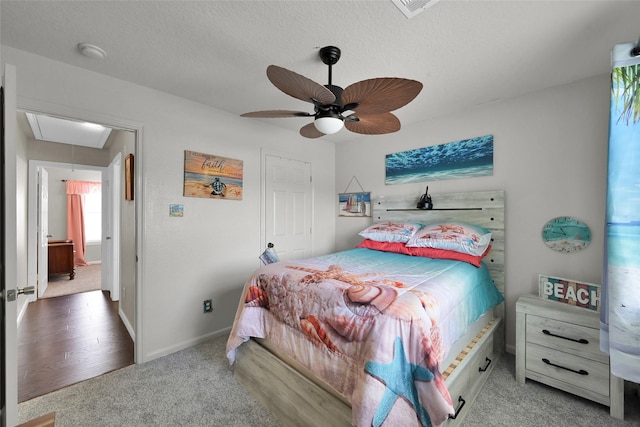 bedroom featuring ceiling fan, a textured ceiling, carpet floors, baseboards, and attic access