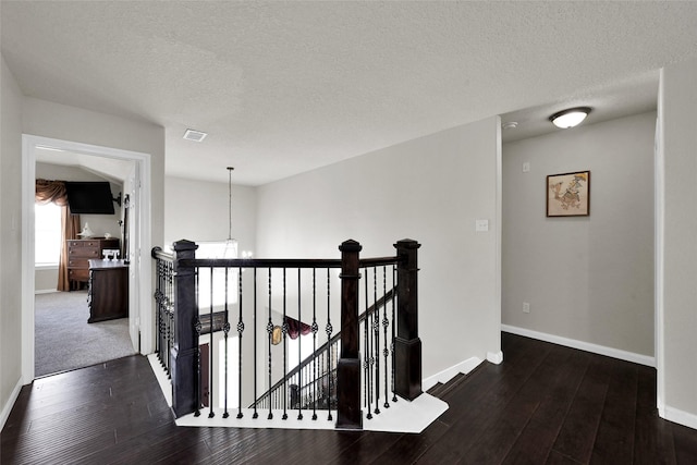 corridor with dark wood-style floors, a textured ceiling, an upstairs landing, and baseboards