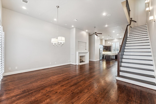 unfurnished living room with recessed lighting, dark wood-type flooring, a fireplace, a ceiling fan, and stairs