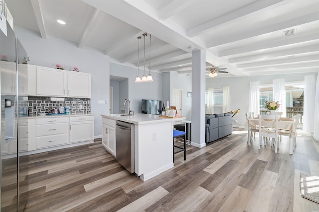 kitchen with light countertops, stainless steel dishwasher, open floor plan, white cabinets, and a sink